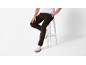 Man in bruine corduroy broek en witte sneakers, zittend op een witte kruk.