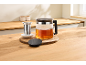 Glazen theepot met thee en theezeef op een houten tafel.