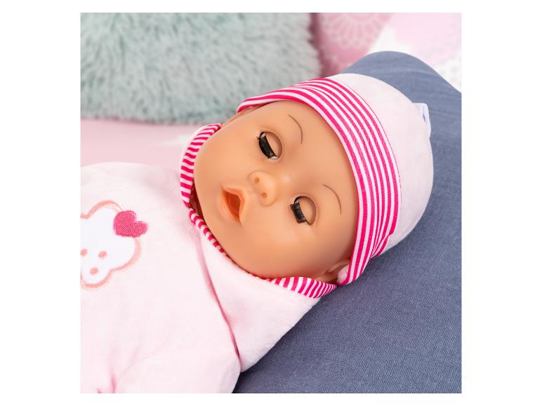 Babypop in roze pyjama en gestreepte muts, liggend op een blauw oppervlak.