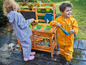 Twee kinderen spelen met water en zand in een houten speelkeuken.
