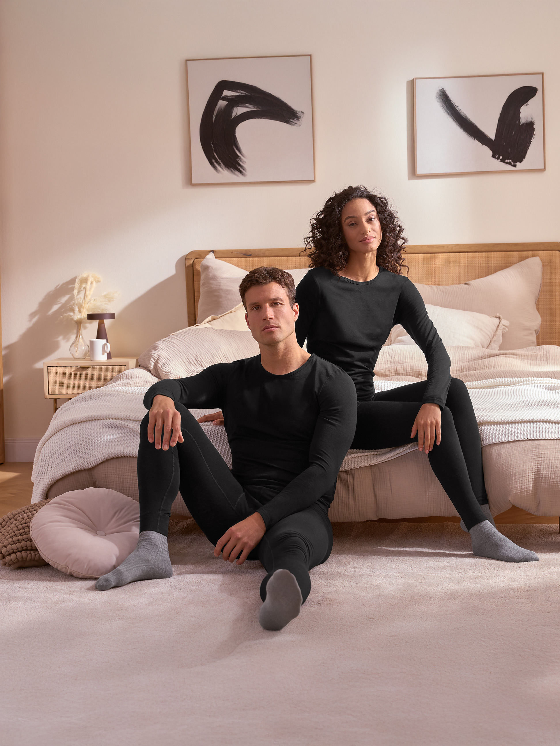 Een stel in zwart thermisch ondergoed zit op de vloer voor een bed.