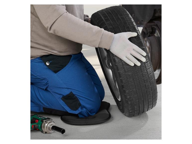 Persoon in blauwe overall en handschoenen verwisselt een band, met gereedschap op de grond.