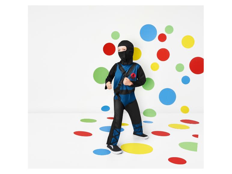 Een kind in een ninja-kostuum staat op een vloer met gekleurde stippen.