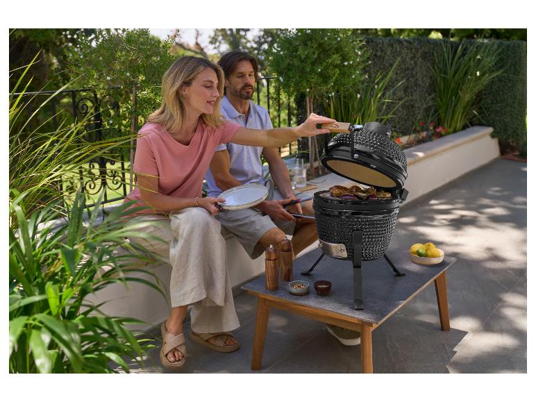 Een stel grilt vlees en groenten op een kamado barbecue buiten.
