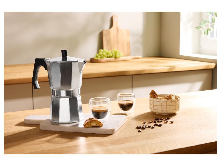 Aluminium mokkapot met twee kopjes koffie, koekjes en koffiebonen op een houten tafel.