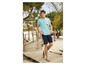 Man in een turquoise T-shirt met palmbomenprint en blauwe shorts op een houten vlonder.