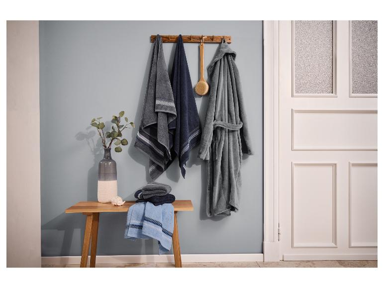 Badkamer met handdoeken, badjas en een houten bankje met vaas en schelp.