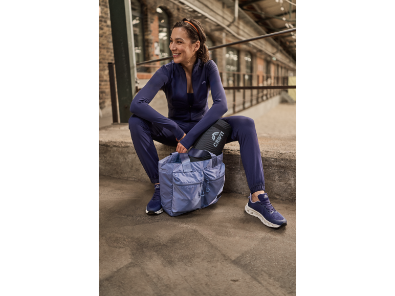 Vrouw in sportkleding zit met een fitnesstas en een yogamat.