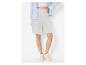 Vrouw in lichtgrijze shorts, witte crop top, blauw gestreept overhemd en witte sneakers.