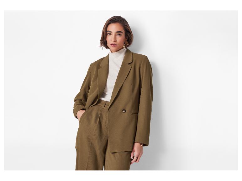 Vrouw in een olijfbruin pak met blazer en broek, draagt een crèmekleurige coltrui.