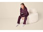 Meisje in donkerpaars velours set met hoodie en broek, zittend op een witte fauteuil.