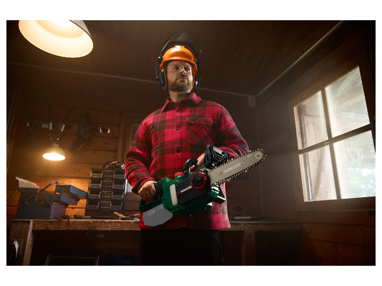 Een man in een rood geruit overhemd houdt een Parkside kettingzaag vast in zijn werkplaats.