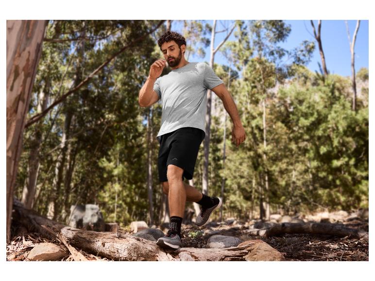 Man in grijs T-shirt en zwarte korte broek trailrunnend in een bos.