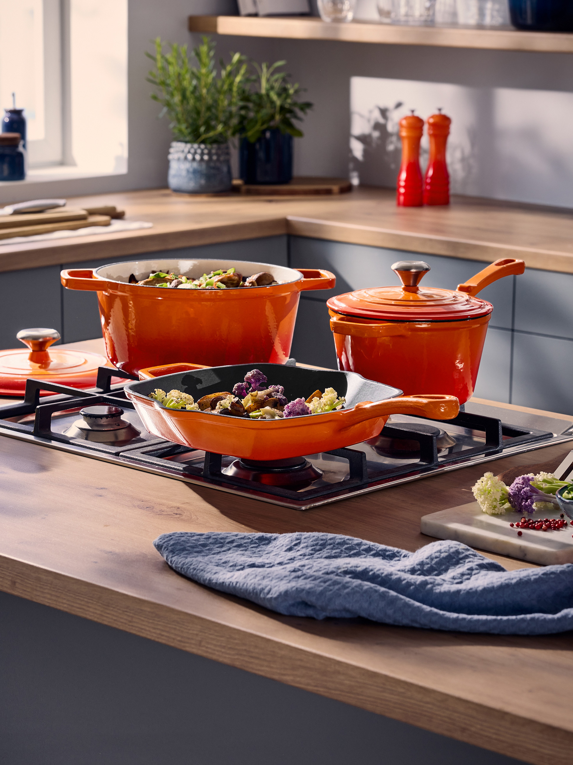 Oranje potten en pannen op een gasfornuis in een moderne keuken.