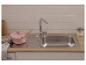 Roze pan met houten lepel bij een gootsteen met kraan en witte tegels.