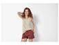 Lachende vrouw met krullend haar, draagt een beige top en bruine shorts.