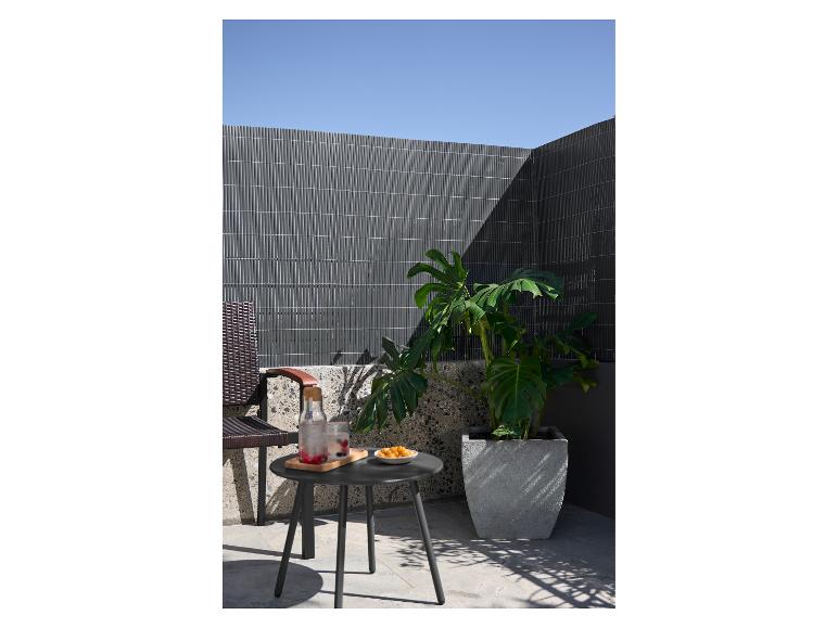 Donkergrijze salontafel met drankjes en snacks op een balkon met een plant.