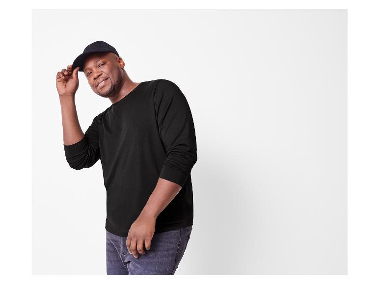 Lachende man in een zwart shirt met lange mouwen en een zwarte pet.