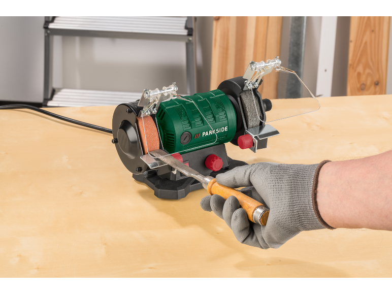 Groene bankslijpmachine met een houtbeitel die wordt geslepen door een gehandschoende hand.