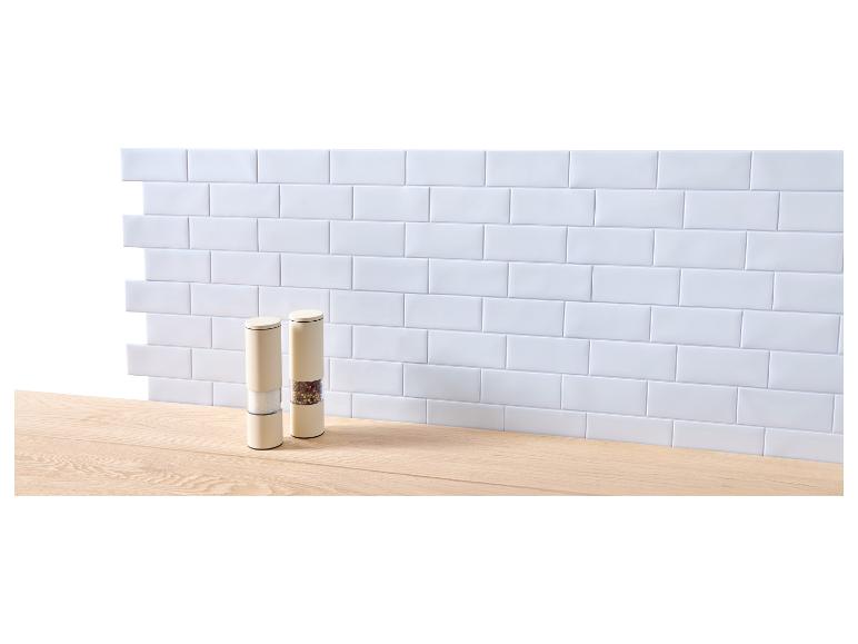 Twee zout- en pepermolens op een houten aanrecht voor een witte tegelmuur.