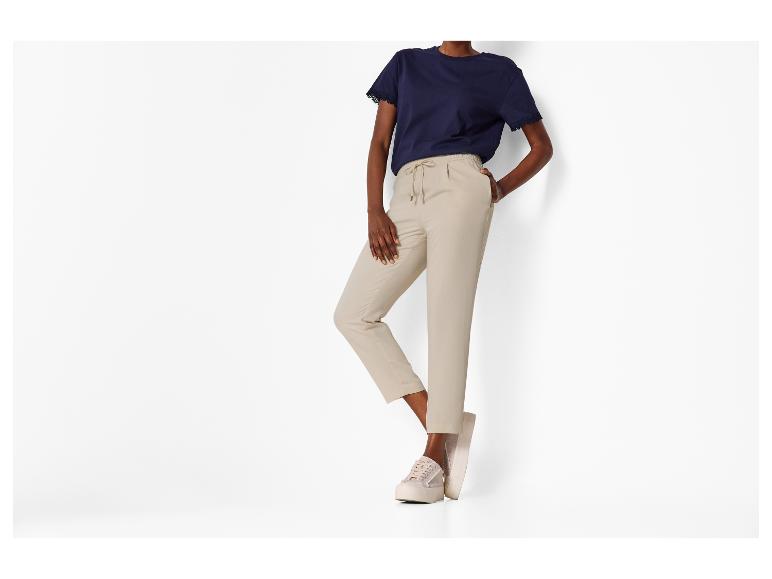 Vrouw in marineblauw T-shirt met kant en beige broek met trekkoord, met beige sneakers.