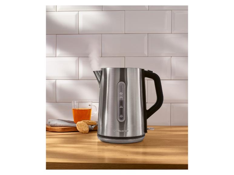 Roestvrijstalen waterkoker met stoom, naast een kopje thee en koekjes.