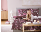 Vrouw leest in bed met bordeauxrood bloemenbeddengoed en bijpassende kussens.