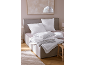 Wit beddengoedset met kussens en dekbedden op een bed in een neutraal getinte slaapkamer.