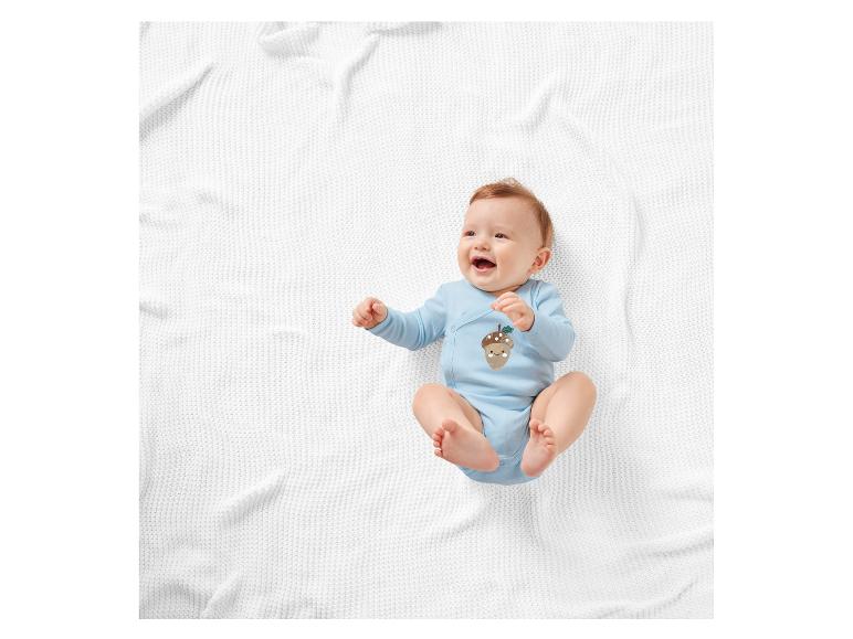 Lachende baby op een witte deken in een lichtblauw rompertje met eikelprint.