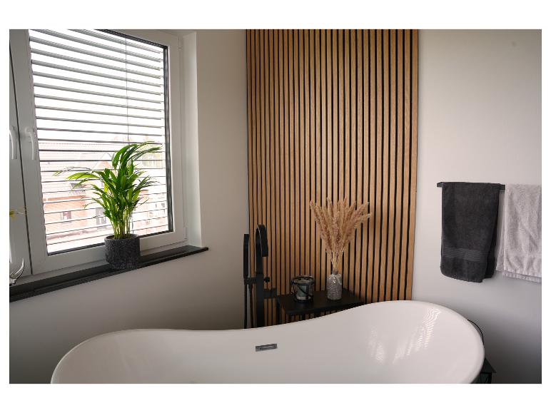 Moderne badkamer met vrijstaand bad, houten lattenwand en groene plant.