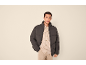 Man in donkergrijze pufferjas, beige corduroy overhemd en beige broek.