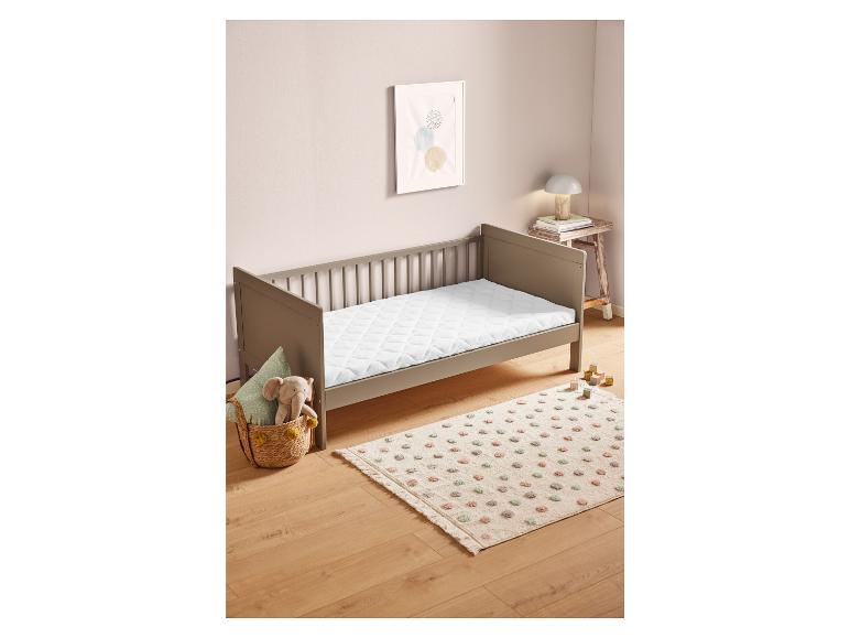 Een wit kinderbed met een matras, een vloerkleed met stippen en een mand met een knuffel.