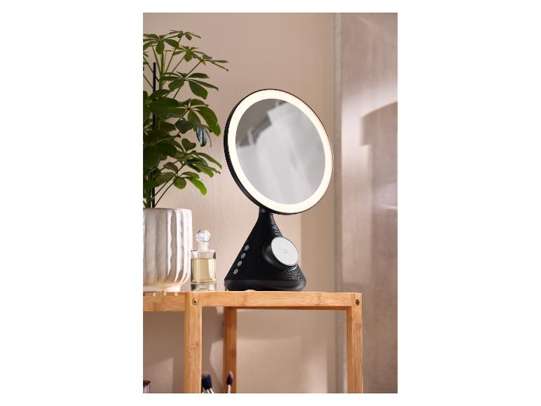 Verlichte make-upspiegel met Bluetooth-luidspreker op houten plank met plant en parfum.