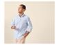 Man in blauw gestreept overhemd en beige broek, met bril in de hand.
