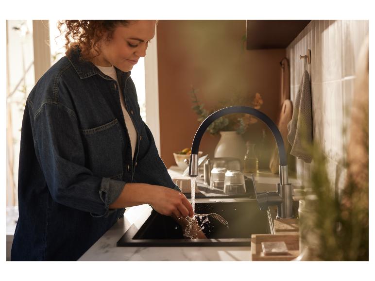 Een vrouw wast de afwas in de keuken onder een moderne kraan.