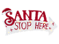 Wit pijlvormig bord met rode tekst 'SANTA STOP HERE' en kerstmuts, verlicht door lampjes.