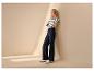 Vrouw in gestreept shirt en wijde jeans leunt tegen een muur, met sneakers aan.