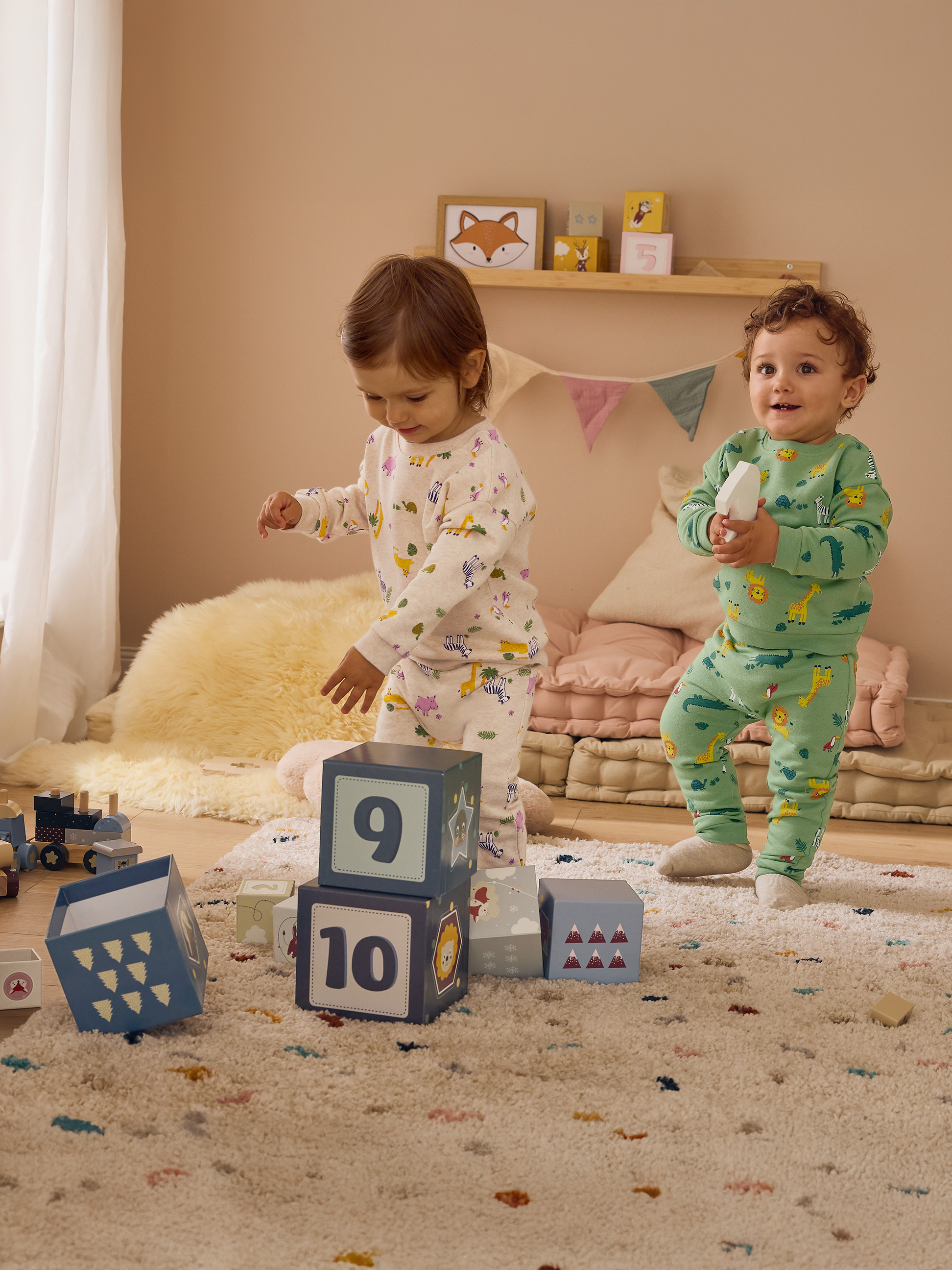 Twee kinderen in pyjama's met dierenprint spelen met blokken in een kamer.