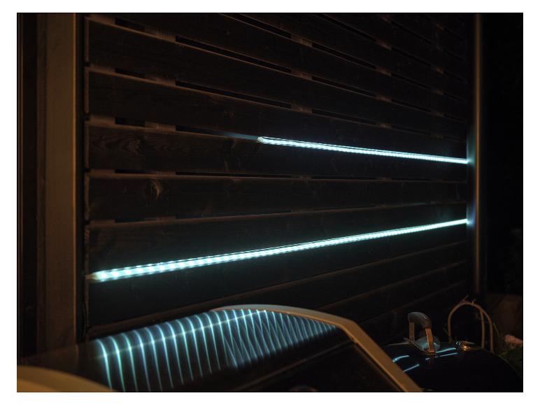 LED-verlichting op houten schutting, reflecterend op grilldeksel.