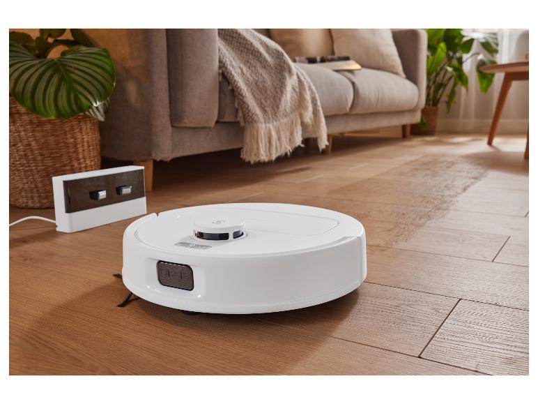 Een robotstofzuiger op een houten vloer in een woonkamer.