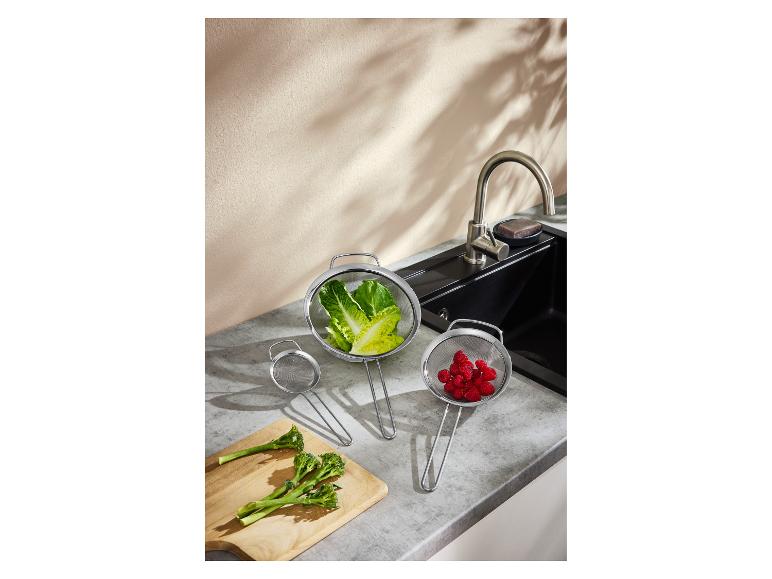 Zeefjes met sla en frambozen, met broccoli op een snijplank naast de gootsteen.