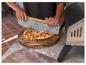 Persoon snijdt een versgebakken pizza met een grote pizzaroller op een houten plank.