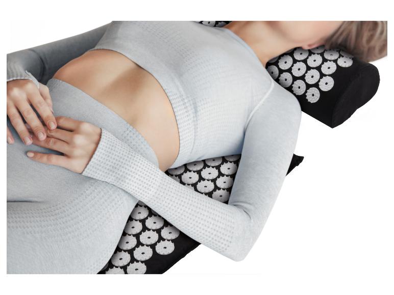 Vrouw ligt op een acupressuurmat en kussen in lichtgrijze sportkleding.