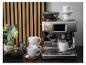 Espressomachine met witte kopjes, koffiebonen en bloemdecoraties op een aanrecht.