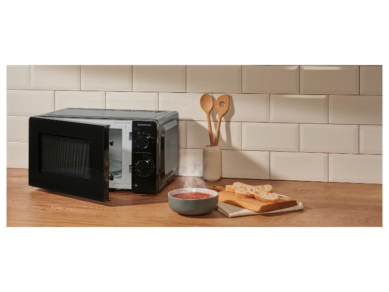 Zwarte magnetron op een houten aanrecht met een kom stomende soep en brood.