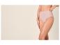 Vrouw in beige hoge slip, met hand op heup, tegen een lichte achtergrond.