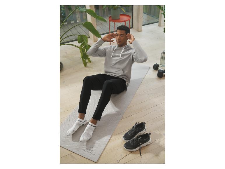 Een man doet crunches op een yogamat, met sneakers en dumbbells naast hem.