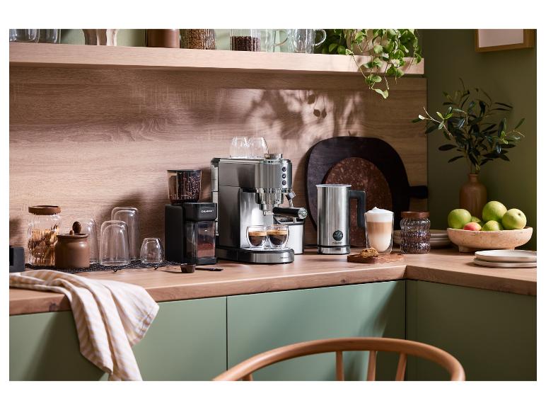 Koffiezetapparaat en molen op een houten aanrecht met groene kasten en planten.