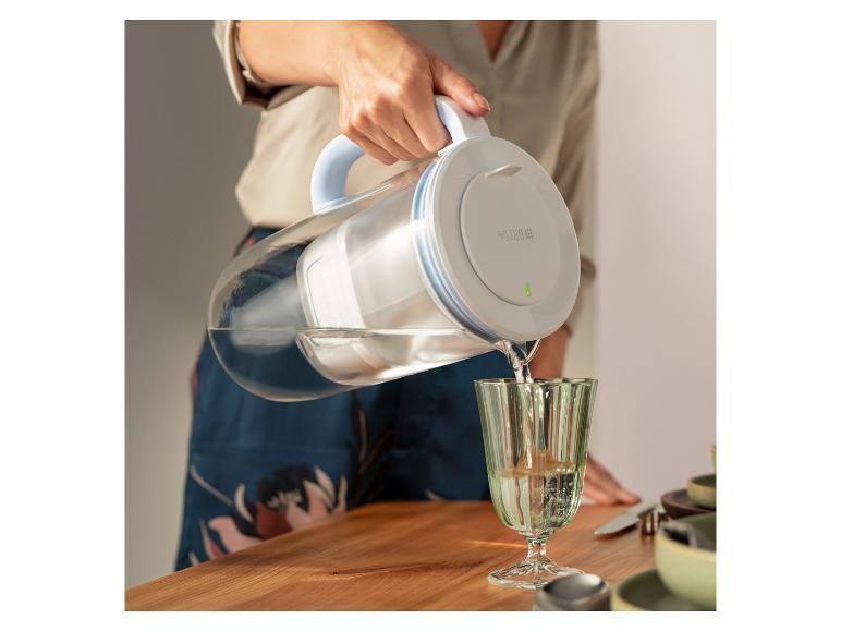 Glazen BRITA waterfilterkan schenkt water in een glas op een tafel.