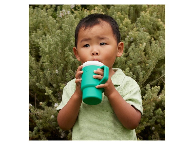 Een klein kind drinkt uit een groene beker met handvat.